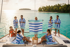 Group of people on a boat wearing matching blue and white striped towels with a tropical island in the background.