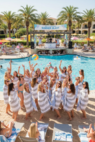 Group of people by a pool with palm trees and a 'Summer Blast' sign in the background.
